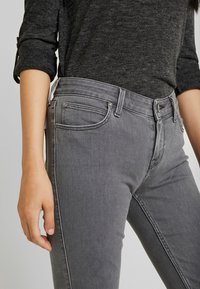 Jeans de mezclilla gris con un ajuste slim, diseño de cinco bolsillos, costuras blancas en contraste y talle medio. Textura suave con un ligero estiramiento.