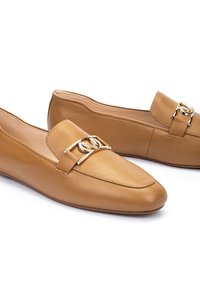 Mocassins en cuir tan avec un bout arrondi, arborant un accent en métal doré sur le dessus. Texture lisse et silhouette simple.