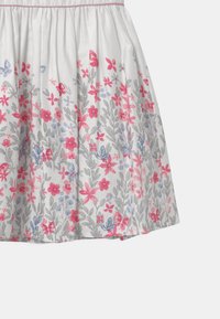 Gonna floreale in cotone bianco, con fiori e foglie rosa, blu e grigi. Vita arricciata con una consistenza morbida e una forma fluida.