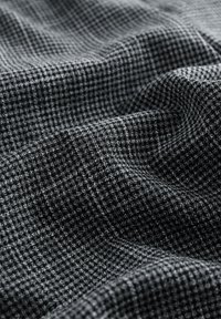 Tessuto testurizzato in nero e grigio caratterizzato da un motivo a quadri, con morbide cadute e un leggero luccichio, che mette in evidenza il materiale intrecciato.