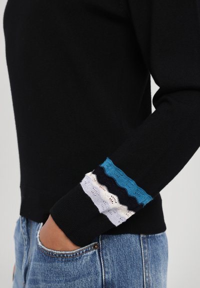 Svart genser med teksturerte, bølgende mansjetter i teal, marineblått, hvitt og lysegrått. Tettsittende design med en uformell silhuett.