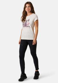 Lichtbeige t-shirt met een roze grafisch ontwerp voor buitenexpedities, gecombineerd met zwarte strakke broek met ritszakken en een gestructureerde stof.