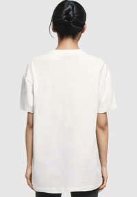 Hvid bomulds t-shirt med korte ærmer, afslappet pasform, rund hals og en ensartet tekstur. Vist fra ryggen.