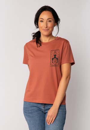 Roodgekleurde katoenen t-shirt met korte mouwen, met een zwarte grafische print van een vrouw en een leeuw, tekst "STERKTE" en sterren.