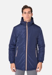 Giacca imbottita blu navy con cappuccio, dotata di una zip a lunghezza totale con dettagli arancioni e due tasche laterali con zip. Texture liscia.