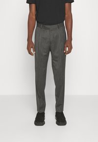 Szare spodnie w prążki wykonane z tkaniny o gładkiej fakturze, z paskiem w talii i dopasowanym krojem. Noszone z czarnym T-shirtem i czarnymi butami.