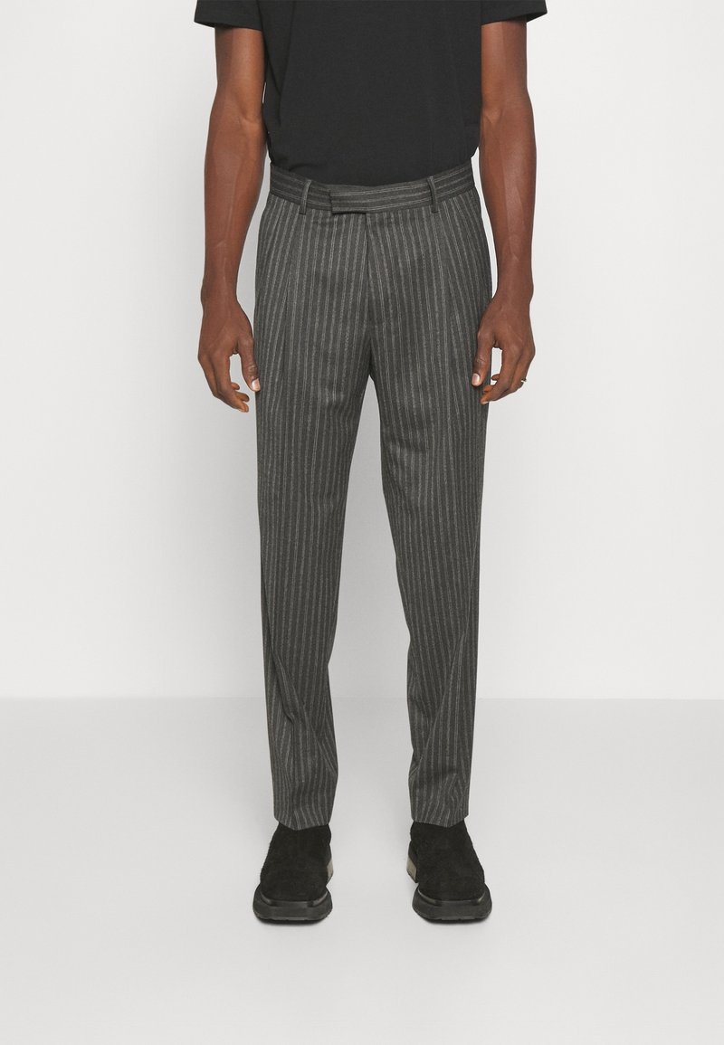 Szare spodnie w prążki wykonane z tkaniny o gładkiej fakturze, z paskiem w talii i dopasowanym krojem. Noszone z czarnym T-shirtem i czarnymi butami.