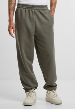 Lätta, olivgröna sweatpants med elastisk midja, avslappnad passform, sidofickor och subtil logotypdetalj. Kombineras med beige sneakers.