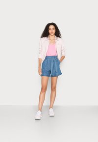 Camisa rosa clara de botões, top rosa em V e calções de ganga azuis de cintura alta com um cinto de laço. Ténis brancos completam o visual.