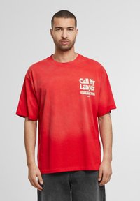 Rød oversized bomulds t-shirt med et hvidt grafisk tryk, der viser "Ring til min advokat" med et telefonnummer nedenunder. Korte ærmer, rund halsudskæring.