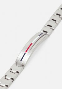 Montre en acier inoxydable avec une finition brossée, présentant un design de maillons courbés et des accents de rouge, blanc et bleu dans un motif élégant.