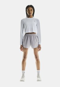 Lätt långärmad vit topp och grå idrottsshorts med elastisk midja. Bärs med vita strumpor och löparskor.