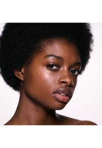 Kvinde med naturlig afrofrisure og glat hud kigger let til siden mod en ensfarvet hvid baggrund.