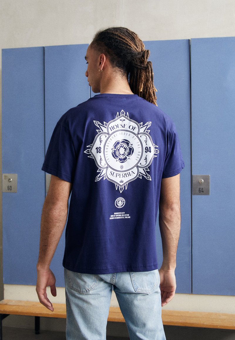 Navy blue cotton t-shirt featuring a large white graphic design on the back with text and emblem details. Short sleeves, relaxed fit.