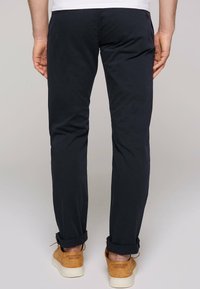Chino scuri blu con vestibilità slim, con risvolti e un tessuto leggero e liscio. Indossati con scarpe beige stringate.