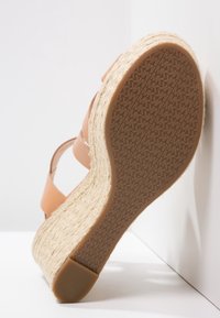 Sandalia cuña marrón con tacón cubierto de yute, suela de goma y tiras entrelazadas. Material superior liso y patrón de suela texturizado.
