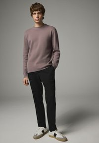 Un pull violet clair, un pantalon noir et des baskets blanches avec des accents gris et noirs. Le pull a un col rond et des poignets côtelés.
