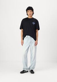 Black cotton t-shirt with a graphic logo, paired with light blue wide-leg jeans and black sneakers with white accents. Simple design.