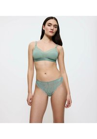 Soutien-gorge vert clair en tissu lisse avec des bretelles ajustables, associé à un string en dentelle assorti avec un motif floral et des bords festonnés.