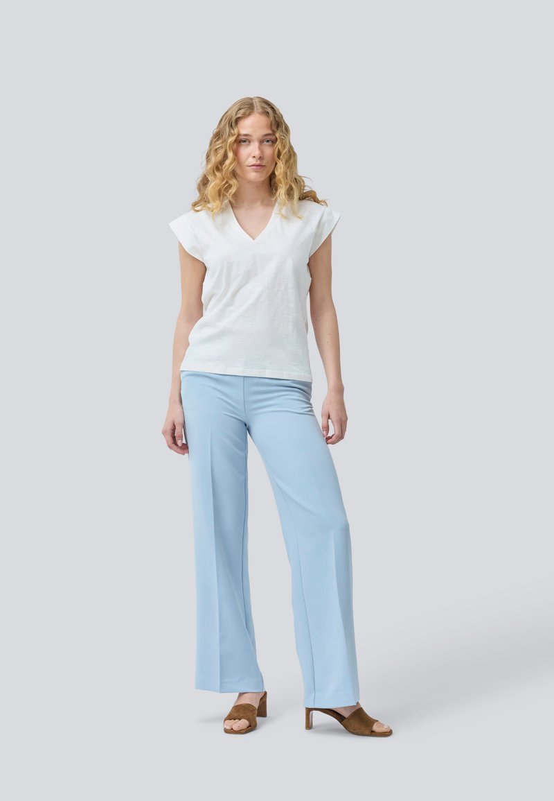 Haut blanc à col en V et à manches courtes associé à un pantalon large bleu clair et des talons ouverts marron. Tissu lisse avec une coupe décontractée.