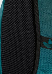 Zaino teal con un motivo esagonale testurizzato, tessuto in rete nera e bordi in nero a contrasto con un accento del logo.