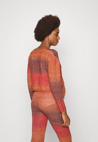 Conjunto de dois peças tricotado com um suéter cropped e calças justas. Degradação gradual de tons de vermelho e laranja com uma textura suave.