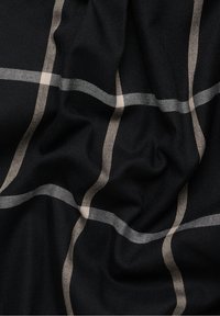 Tissu noir avec motif à carreaux beige, présentant une texture douce et un drapé fluide, mettant en valeur des lignes épaisses et fines alternées.