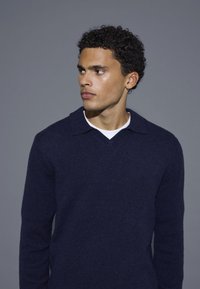 Dunkelblauer, gestrickter Pullover mit V-Ausschnitt und Kragen, aus weichem Material, mit strukturierter Oberfläche und taillierter Passform.