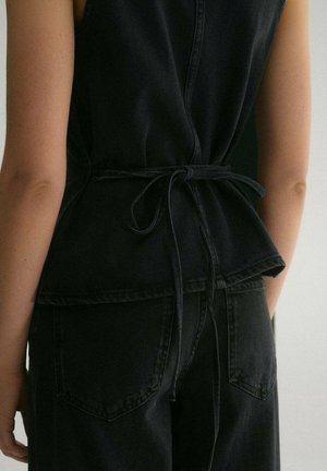 Černý denimový oděv s opaskem v pase, s peplumovým střihem. Pozoruhodný svou texturou a zadními kapsami, viděný zezadu.