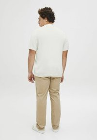 Camisa de punto blanca con textura y mangas cortas combinada con pantalones beige, vista desde atrás. Los pantalones son de corte recto con un dobladillo sutil.