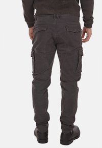 Pantaloni cargo grigi con tasche posteriori, vita regolabile e una finitura elegante e testurizzata. Abbinati a calzature nere.