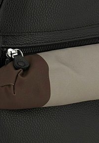 Bolso de cuero negro con textura, que presenta un acento de tela marrón y gris y un bolsillo con cremallera. El herraje de cremallera visible mejora la funcionalidad.