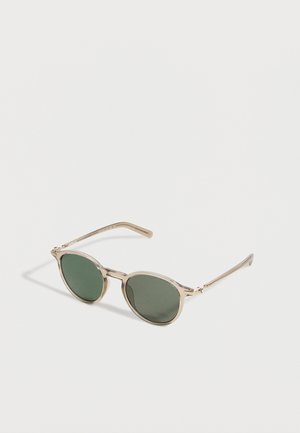 Round sunglasses with thin transparent beige frames and dark green lenses, laid flat on a white surface with shadows.