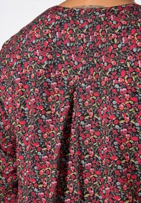Textil s květinovým vzorem v odstínech červené, růžové a modré na černém pozadí; obsahuje skládací design s malými květinami a zelenými listy.