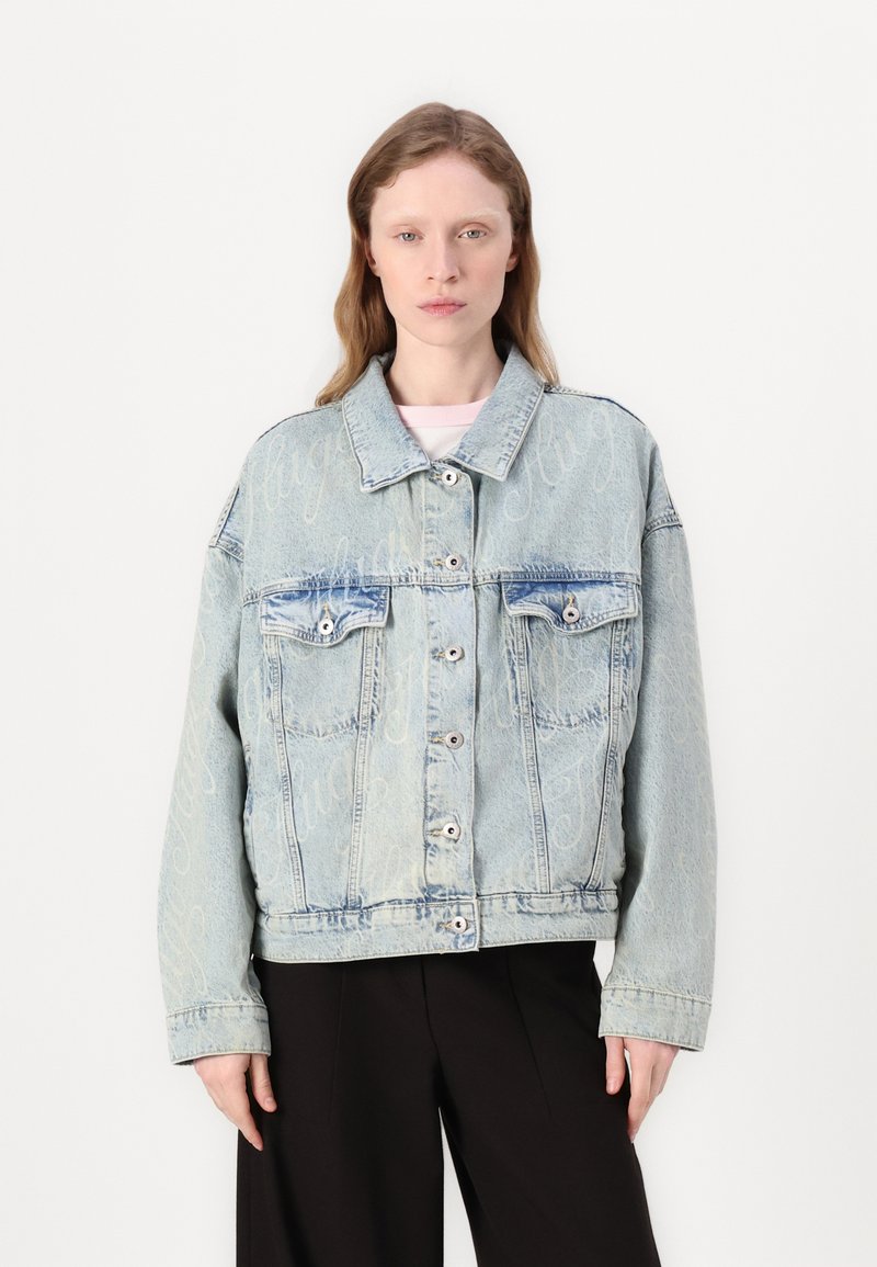 Light blue denim jacket with a relaxed fit, featuring double breast pockets, button closure, and subtle embossed lettering on the fabric.