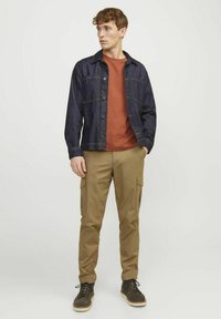 Spijkerjack met knoopsluiting, oranje t-shirt en beige cargobroek; gestyled met donkerbruine veterschoenen en een textuurstof.