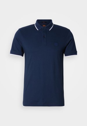 Polo azul marino con cuello clásico, tapeta con dos botones y detalles contrastantes blancos en las mangas. Incluye un parche con el logo en el pecho.