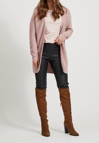 Světle růžový kardigan s dlouhými rukávy, pruhované tričko, černé legíny a hnědé semišové boty nad kolena s robustním podpatkem.