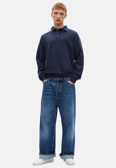 Polo a maniche lunghe blu navy con colletto e dettagli in bottone abbinato a jeans chiari larghi e sneaker bianche.