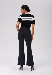 Svart vide jeans med høy midje, designet med to baklommer. Kombinert med en svart og hvit stripet topp med korte ermer.