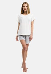 Witte katoen T-shirt met korte mouwen en een bedrukte ontwerpen, gecombineerd met lichtgrijze shorts met een stippenpatroon.