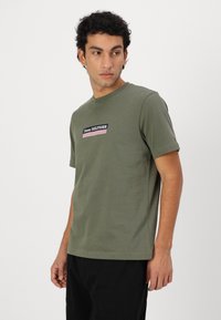 Olive green short-sleeve t-shirt made of soft cotton. Features a rectangular logo patch with "Tommy HILFIGER" and striped accents.