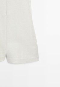 Partie basse d’un short en tissu blanc uni avec une petite fente sur chaque jambe sur fond blanc.