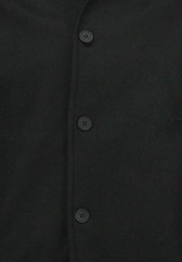 Zwarte gebreide cardigan met een knoopsluiting aan de voorkant en vier zwarte knopen. Zachte textuur met een eenvoudig, effen ontwerp.