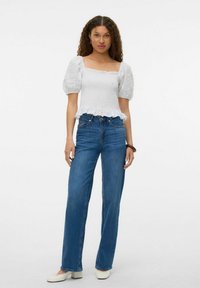 Top bianco con maniche a sbuffo in tessuto testurizzato e bordo arricciato, abbinato a jeans blu a vita alta e gamba dritta e scarpe bianche.