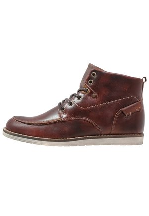 Stivaletto alla caviglia in pelle marrone con lacci anteriori, occhielli in metallo, dettagli cuciti e suola in gomma beige.