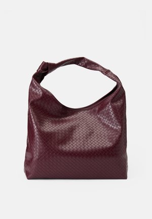 Große weiche bordeauxrote Handtasche mit gewebter Lederstruktur und einem breiten, oben geschlungenen Tragegriff vor einem einfarbigen hellen Hintergrund.