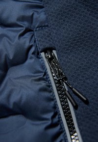 Tessuto di giacca blu navy con una texture liscia, caratterizzato da una chiusura con zip con accessori neri e accenti grigi vicino alla cucitura.