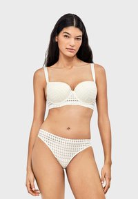 Ensemble bikini en dentelle blanche, composé d'un soutien-gorge structuré aux bords festonnés et d'un string taille haute assorti, mettant en valeur des motifs ajourés complexes.
