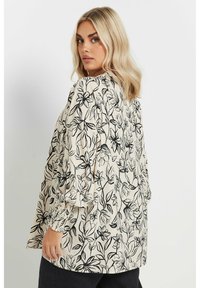 Blommig blus i krämfärgad med svarta botaniska mönster. Har puffärm och elastiska manschetter för en avslappnad passform.